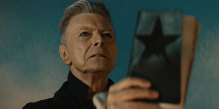 David Bowie che tiene in mano un libro con una Blackstar in copertina