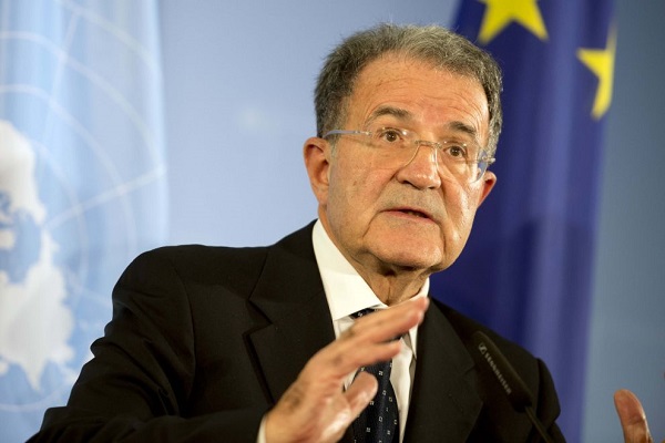 referendum grecia romano prodi con la mano destra alta parla con dietro una bandiera dell'europa