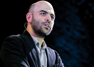 primo piano di roberto saviano con sfondo scuro alle spalle