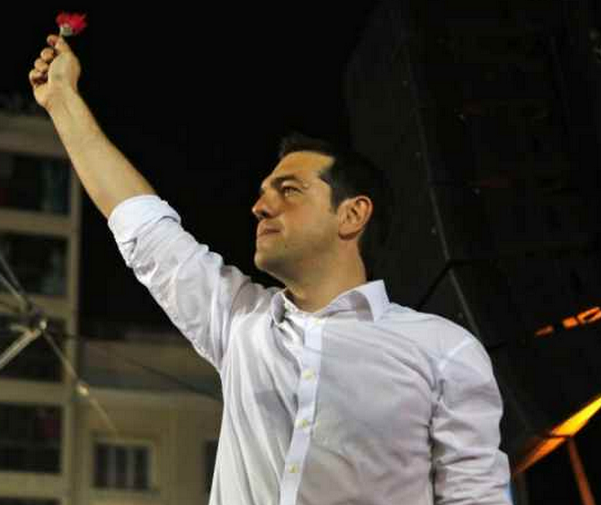 tsipras sul palco in camicia bianca e fiore in mano