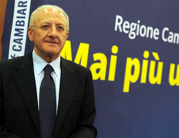 de luca con dietro un manifesto della sua campagna elettorale e lo slogan 'mai piu ultimi'