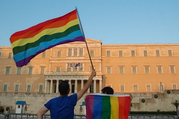 Diritti LGBT, Grecia, Italia, due persone con la bandiera dei diritti lgbt davanti ad un ministero greco