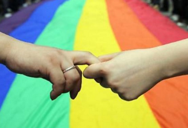 unioni civili, l'immagine di due mani che si avvicinano e sullo sfondo la bandiera coi colori arcobaleno