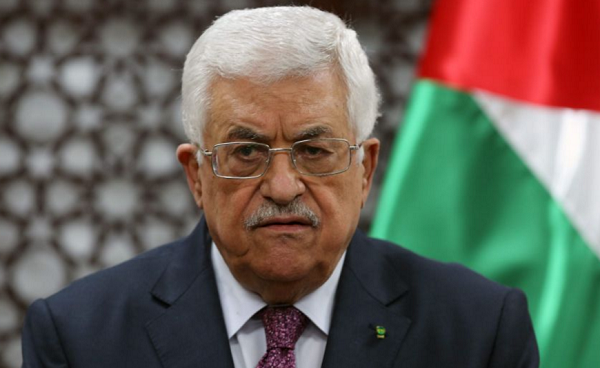 Mahmoud Abbas ritratto in foto con abito, camicia chiara e cravatta scura. Alle sue spalle la bandiera della Palestina
