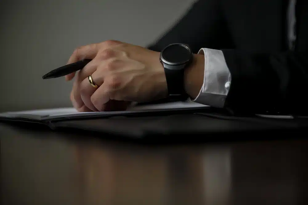 Dettaglio di una persona con in mano una penna ed un orologio scuro al polso