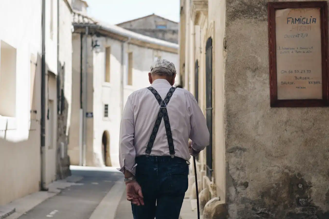 anziano con bastone bretelle scure fotografato di spalle