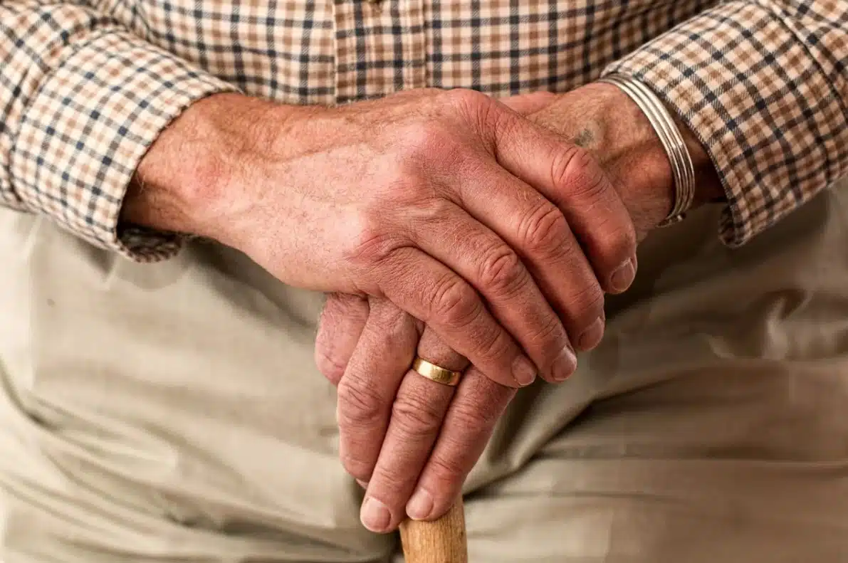 Mani di un anziano una sull'altra con bastone ed anello