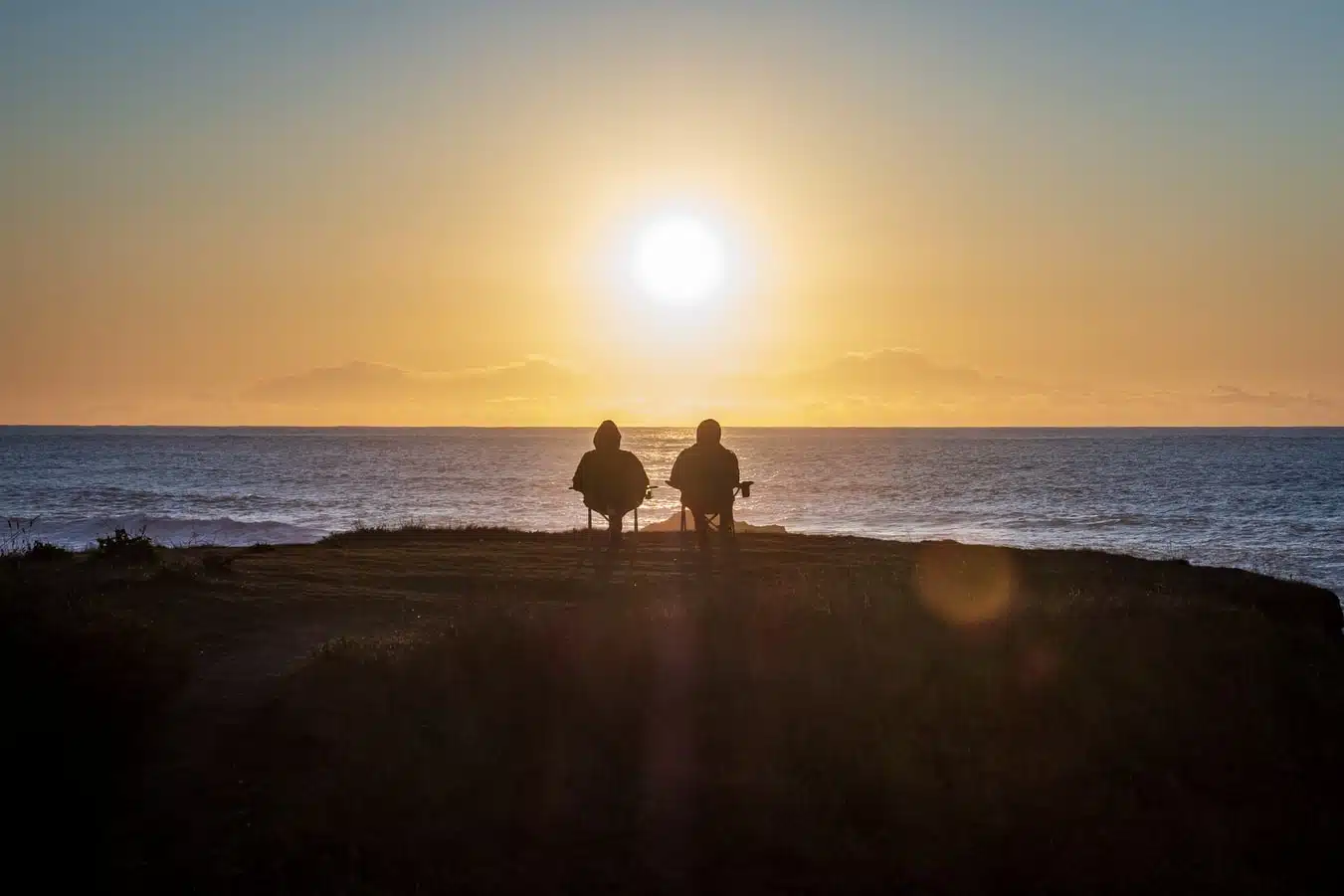 Coppia di anziani seduti davanti ad un paesaggio di mare all'ora del tramonto