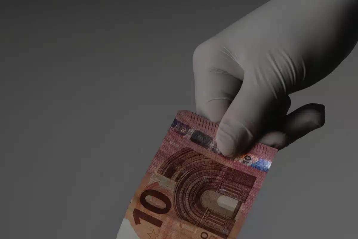 una mano che indossa un guanto in lattice tiene una banconota da 10 euro