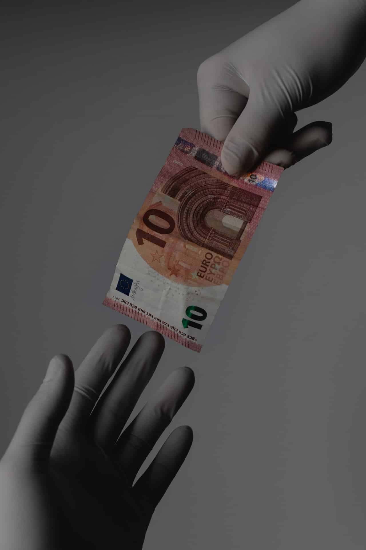 mani che indossano guanti per profilassi da contagio Covid19 si passano una banconota da 10 euro