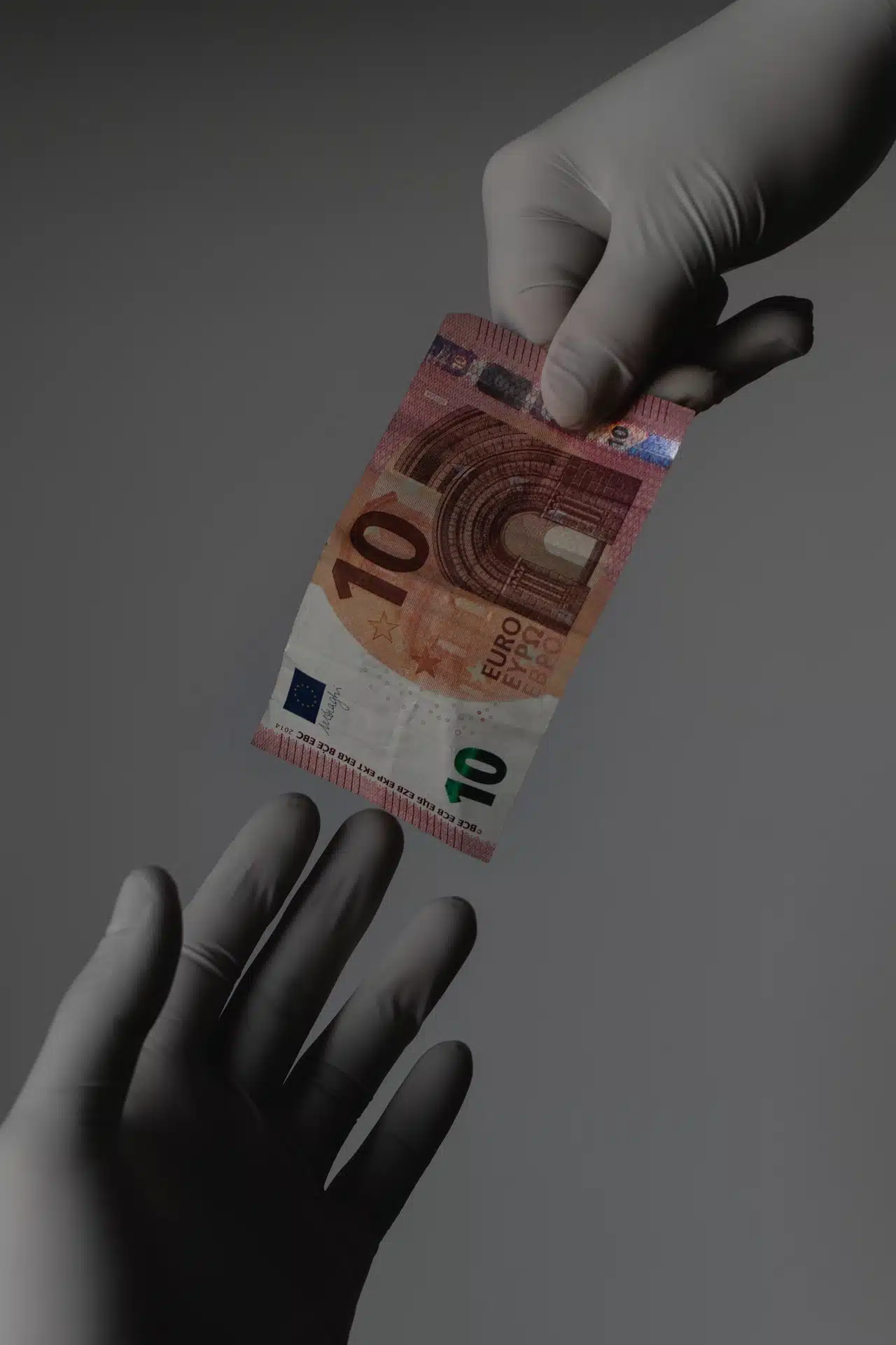 mani che indossano guanti per profilassi da contagio Covid19 si passano una banconota da 10 euro