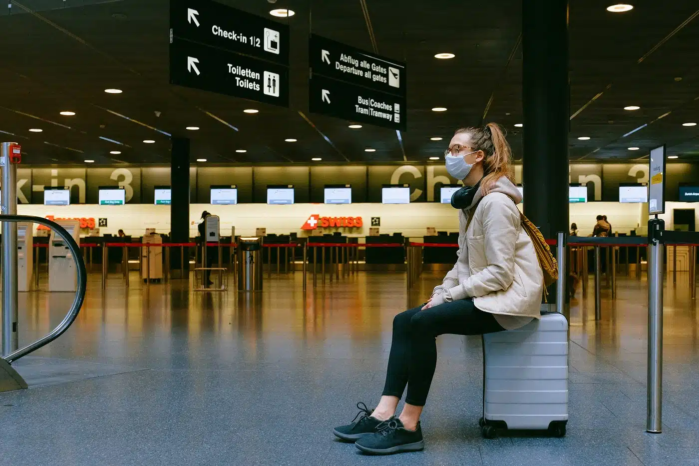 Donna con mascherina seduta su un trolley all'interno di un aeroporto vuoto