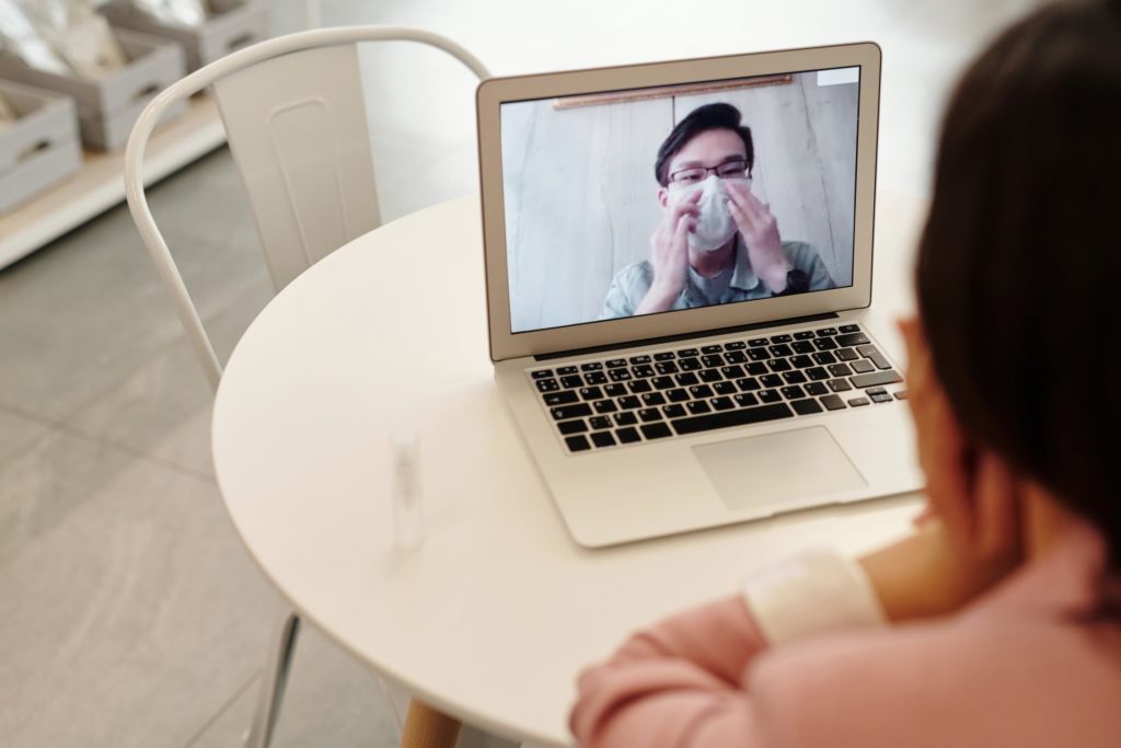 Due persone che dialogano in video tramite il pc. Una persona di spalle e l'altra in video con la mascherina