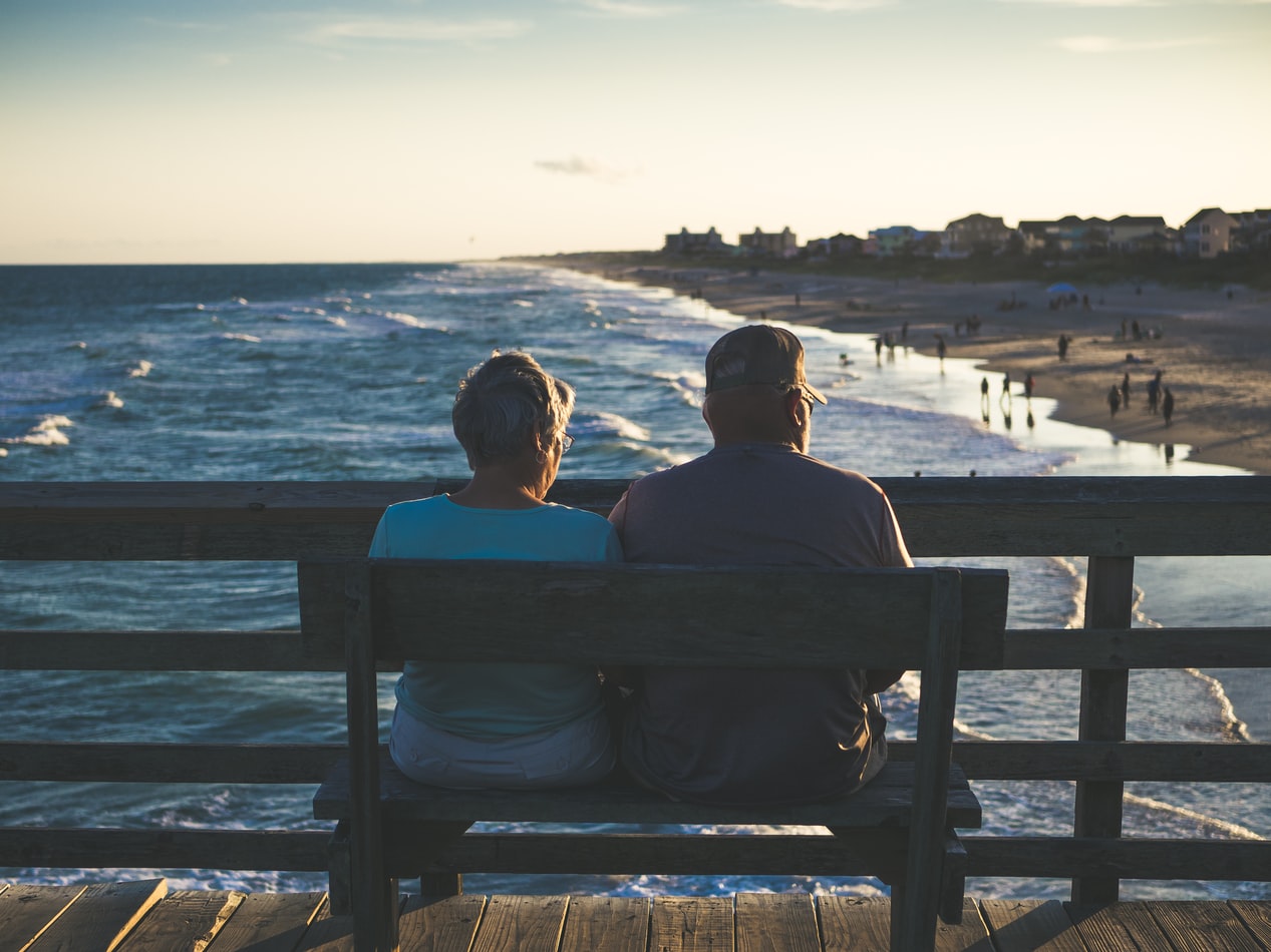 Coppia di anziani di spalle seduti su una panchina di fronte al mare
